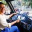 Raquel Lyra sorri olhando na nossa direção enquanto segura com as duas mãos no volante de um ônibus