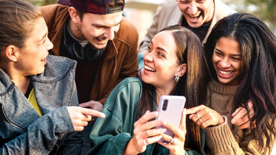 Jovens em volta de um celular rindo entre si