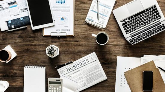 Visão de cima de mesa com vários computadores, agendas, cafés, calculadoras