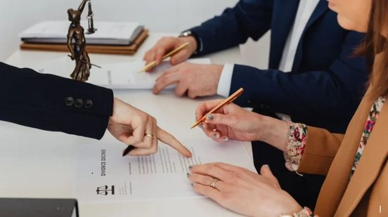 Dama da justiça em uma mesa com pessoas apontando para um papel, uma mulher assina esse papel