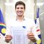João Campos sorri com documento em mãos. Ao fundo bandeira do Recife e de Pernambuco