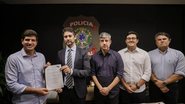 João Campos segura documento ao lado de Victor Marques e outros 3 homens brancos. Ao fundo logo da Polícia Federal
