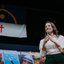 Raquel Lyra falando em microfone com bandeira de Pernambuco ao fundo