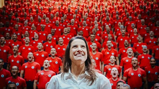 Raquel Lyra sorrindo de costas para uma plateia de bombeiros que gritam