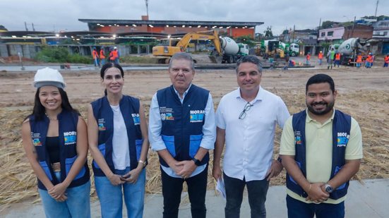 Ricardo Paes Barreto e Túlio Vilaça em frente a uma construção. Duas mulheres e um homem de coletes do governo de Pernambuco sorriem ao lado