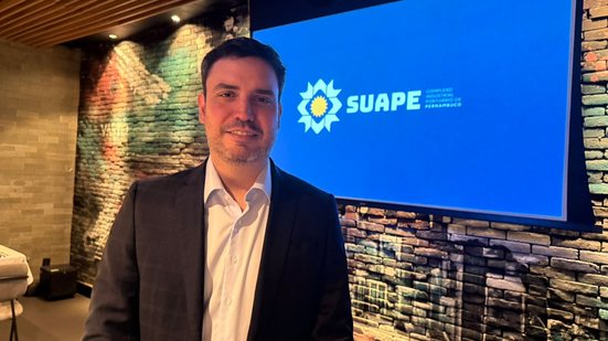 Armando Bisneto em frente a uma tela escrito Suape