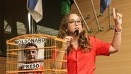 Kari Santos fala em microfone de plenário ao lado de gaiola com a foto de Bolsonaro e escrito "Bolsonaro preso"
