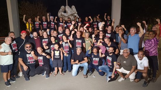 Grupo de pessoas com camisetas pretas escrito "metrô é do povo" com mãos direitas erguidas em punho. Luiz Soares é um deles