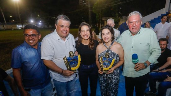 Raquel Lyra e Priscila Krause sorriem com esculturas pequenas de caboclo de lança nas mãos, ao lado três homens sorriem