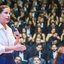Raquel Lyra fala em pé em microfone, ao fundo diversas pessoas estão sentadas usando preto