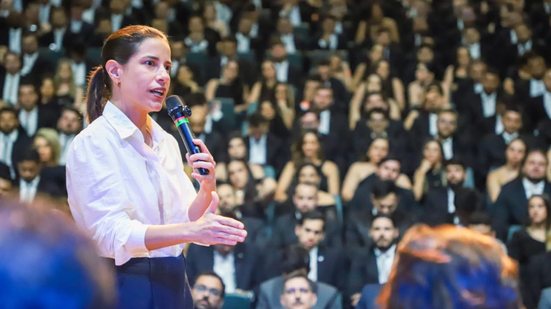 Raquel Lyra fala em pé em microfone, ao fundo diversas pessoas estão sentadas usando preto