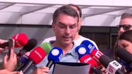 Flávio Bolsonaro lê papel, ao redor diversos microfones de veículos de imprensa