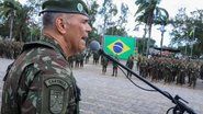 Raquel Lyra ajoelhada sorri enquanto está com as mãos em uma muda de planta recém enterrada, vários homens, alguns com farda do Exército observam
