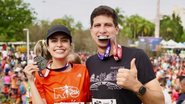 João Campos e Tabata Amaral com roupas de corrida seguram medalhas. João Campos está com medalha na boca, ambos sorriem
