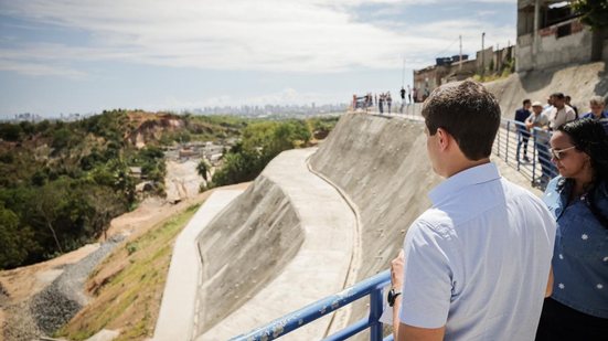 João Campos observa encosta com concreto, diversas pessoas estão proximas