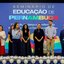 Raquel Lyra, Gilson Monteiro em palco. Raquel fala em microfone. Ao fundo telão escrito "seminário de educação de pernambuco"