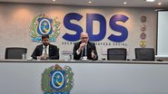 Alessandro e Felipe sentados em mesa com logo do governo de pernambuco, ao fundo simbolo da sds
