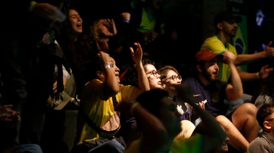 Menina com camisa do Brasil faz feição de assustada enquanto assiste partida