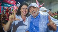 Lula e Simone Tebet sorriem abraçados lado a lado. Simone faz o L com a mão. Lula faz um joinha com a mão. Ao fundo pessoas com roupas vermelhas e simbolos da campanha de 2022
