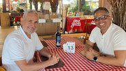 Dois homens sorriem sentados em uma mesa de restaurante