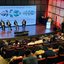 Exposição. Pessoas em palco sentadas em cadeira conversam