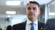 Flávio Bolsonaro lê papel, ao redor diversos microfones de veículos de imprensa