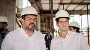 Felipe Cury e João Campos de capacete de construção olham para o lado enquanto conversam