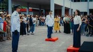 Raquel Lyra em frente a dois homens com farda oficial militarizada. Ao fundo diversas pessoas