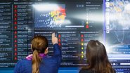 Duas mulheres olham para telão de monitoramento de chuvas da APAC