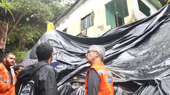 Victor Marques e agentes da Defesa Civil olham para lona