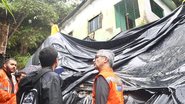 Victor Marques e agentes da Defesa Civil olham para lona