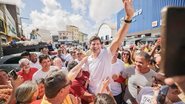 João Campos é levantado por um homem enquanto acena, multidão o segue. Entre pessoas estão Rodrigo Farias e Humberto Costa