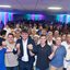 Miguel Coelho, Marcelo Gouveia, Marcio Botelho e outros estão com as mãos erguidas unidas enquanto sorriem. Ao fundo multidão em salão