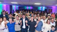 Miguel Coelho, Marcelo Gouveia, Marcio Botelho e outros estão com as mãos erguidas unidas enquanto sorriem. Ao fundo multidão em salão