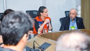 raquel lyra com colete laranja com bandeira de pernambuco costurada no lado esquerdo ao lado de raquel almir cirilo todos estão sentados em mesa de reunião