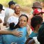 Raquel Lyra abraça mulher, governadora está de olhos fechados. Diversas pessoas de chapéus, algumas do MST estão ao redor. Ao fundo estrada de barro