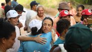 Raquel Lyra abraça mulher, governadora está de olhos fechados. Diversas pessoas de chapéus, algumas do MST estão ao redor. Ao fundo estrada de barro