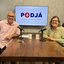 Teresa Leitão e Jamildo estão sentados em frente a microfones, ambos sorriem. Ao fundo tv escrito PodJá