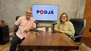 Teresa Leitão e Jamildo estão sentados em frente a microfones, ambos sorriem. Ao fundo tv escrito PodJá