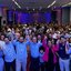 Multidão em auditório levanta as mãos juntos. Na frente estão Felipe Alecrim, Renato Antunes, Romeu Zema, Eduardo Moura e Carlos Sant'anna