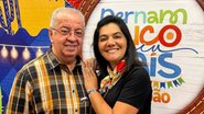 Joselito e Viviane sorriem. Joselito usa roupa xadrez, ela usa um lenço colorido no pescoço com camiseta preta. Ao fundo painel colorido escrito "pernambuco meu paíse são joão"