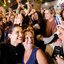 Raquel Lyra posa para selfie com mulher, atrás está Miguel Coelho. Ao fundo diversas pessoas