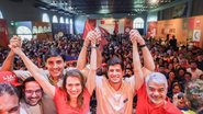 Com as mãos erguidas unidas estão Carlos Costa, Marília Arraes, João Campos e Humberto Costa. Ao fundo multidão. Paredees estão escrito chega junto