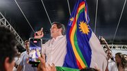 João Campos fala em microfone enquanto segura bandeira de Pernambuco