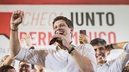 João Campos fala ao microfone enquanto sorri. Ao fundo Carlos Costa e Victor Marques também sorriem. Mais ao fundo escrito "chega junto pernambuco"