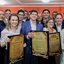 Marília Arraes, João Campos e Teresa Leitão seguram placas grandes de homenagem. Diversas pessoas sorriem ao redor