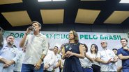 Raquel Lyra olha para Daniel Coelho enquanto ele fala em microfone, também observam mais ao fundo Miguel Coelho, Fernando Dueire, Priscila Krause, Mirella Almeida