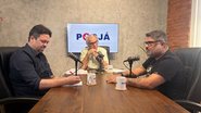Frente a frente em uma mesa estão Felipe Alecrim e Rinaldo Júnior, que estão em frente a microfones de podcast, no meio na ponta da mesa Jamildo observa os dois. Ao fundo televisão com logo do PodJá