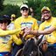 Com camisetas amarelas e chapeus, João Campos, Gabriel Porto e Álvaro Porto sorriem com mãos unidas. Todos estão em cima de cavalos