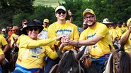 Com camisetas amarelas e chapeus, João Campos, Gabriel Porto e Álvaro Porto sorriem com mãos unidas. Todos estão em cima de cavalos